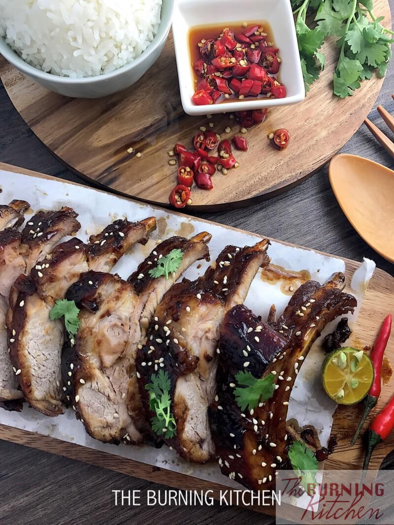 Sticky Chinese Honey Pork Ribs on chopping board, with bowl of rice and bowl of cut chilli with soya sauce on the side