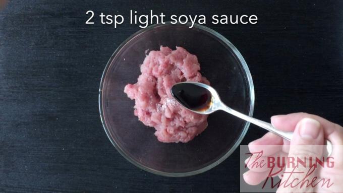 adding a teaspoon of light soy sauce to minced pork in glass bowl