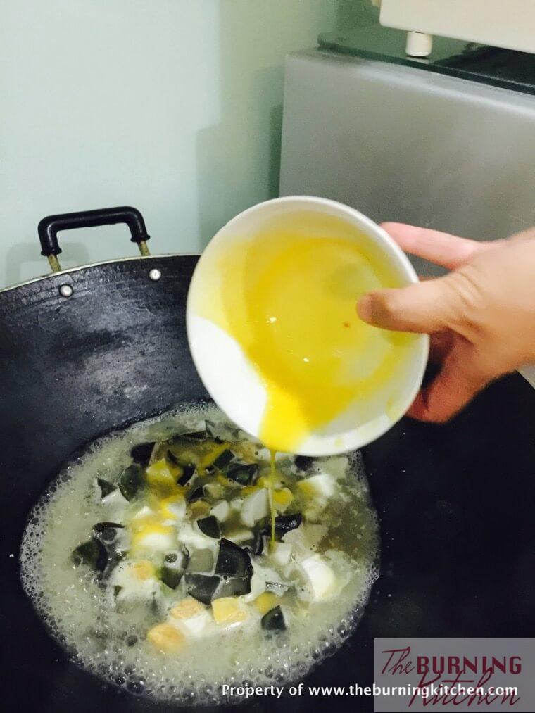 scrambled raw chicken eggs being added into ikan bilis broth with century eggs and salted eggs