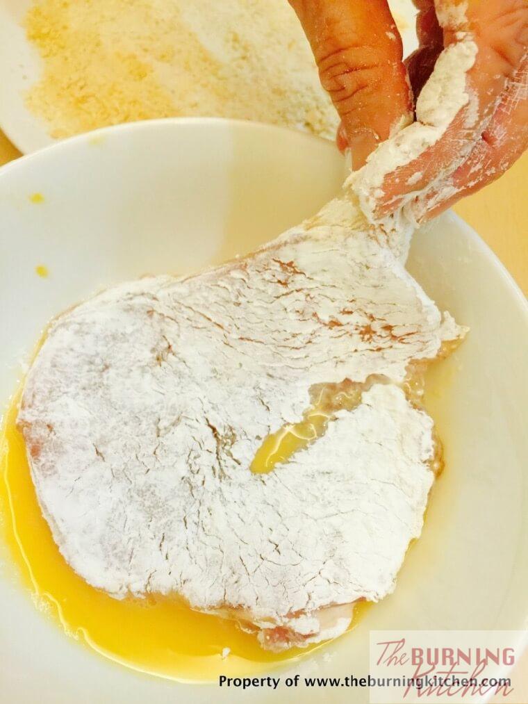 Dipping pork chop coated in corn flour in beaten egg mixture