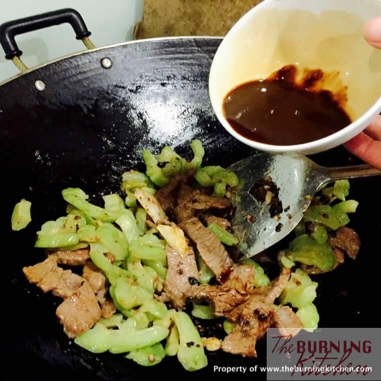 Pour sauce onto sliced bitter gourd and sliced beef in wok