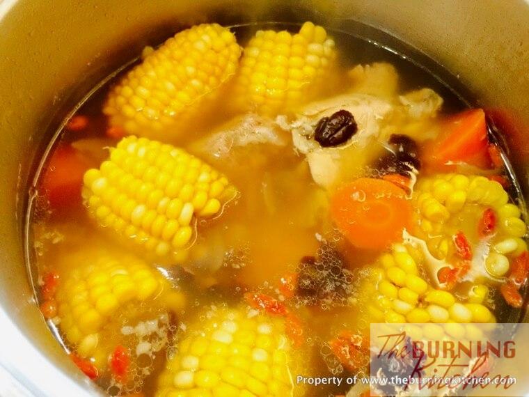 corn, carrots, red dates and wof berries simmering in pork rib broth in big metal pot 