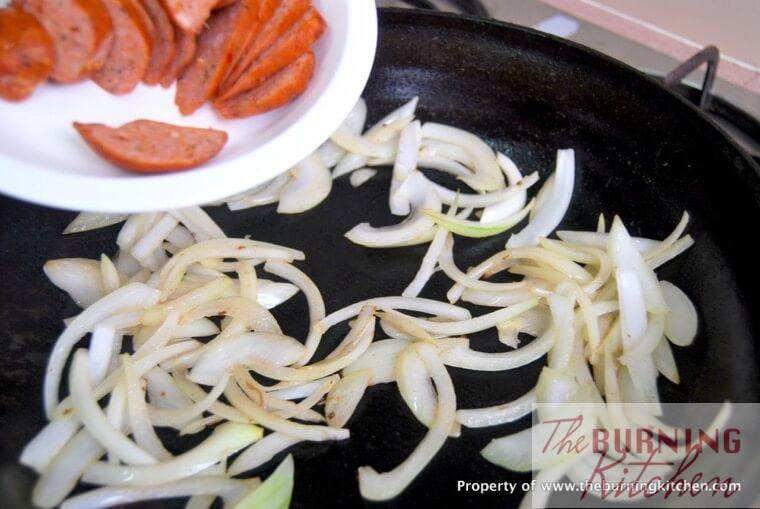 Sautéing sliced onions and chorizo in pan 