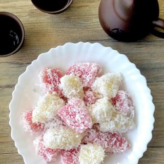 steamed tapioca cake coated in grated coconut on white plate with accompanying chinese tea cup and pot