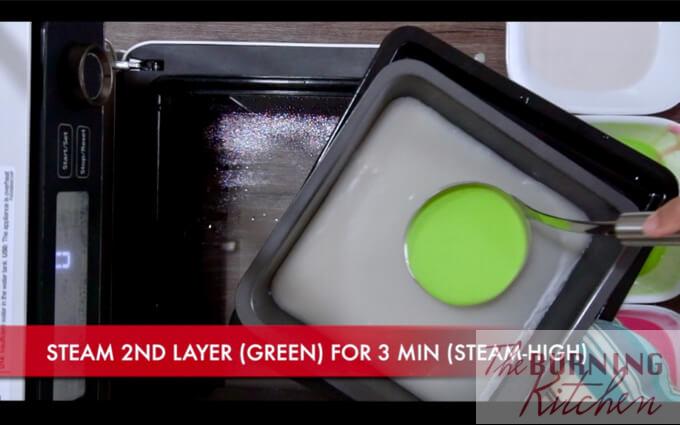 Pouring green batter over white batter in baking tray 