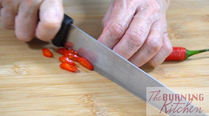 Cutting board with a red chilli being sliced thinly
