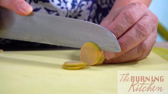 Ginger being sliced thinly on a cutting board