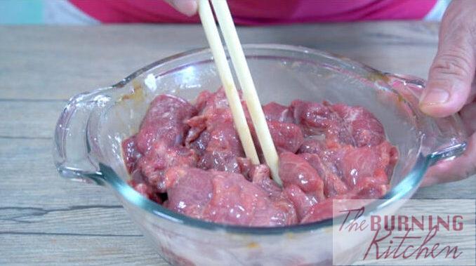 Bowl of raw sliced beef being marinated in a glass bowl