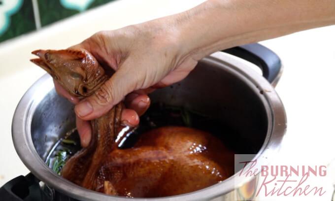 Chicken being lifted out of the pot by holding the neck